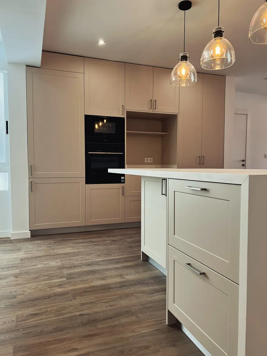 Cocina terminada en tono crema con isla y lámparas colgantes, abierta al salón